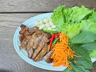 Pork meat grilled with fresh vegetable salad on white plate and wooden background.