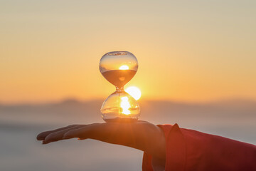 Hand Holding Hourglass with Golden sunrise background, timer , sand , hourglass , gold, symbolizing the passage of time.