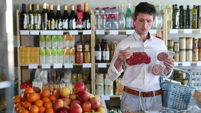 Man choose and buy raw cooled beef entrecote and hamburger cutlet in store. Visitor make choice of assortment, buy raw meat product. Customer read label, examine packaging 