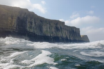 Water splashes against cliffs under a cloudy sky near a coastline in early afternoon light