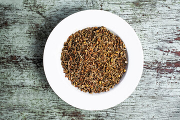 Cumin seeds resting in a white bowl on rustic wooden table