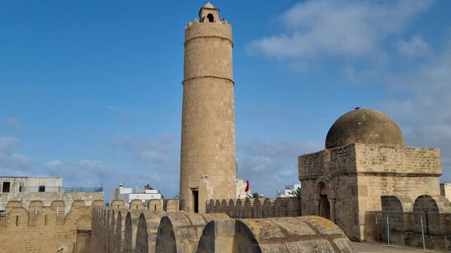 A shot of the Ribat Tower in Sousse on a clear, windy day, with a Tunisian flag fluttering gracefully in the breeze