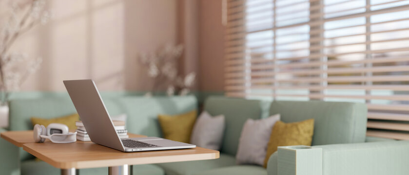A laptop placed on a wooden table in modern pastel cafe or office lounge. - Powered by Adobe