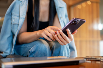 A close-up of a woman in a denim jacket sits in a coffee shop, using her smartphone.
