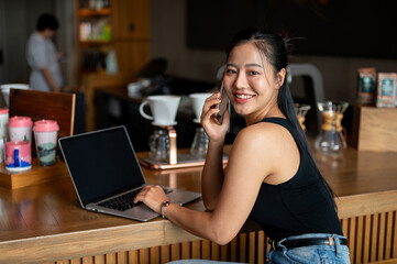 Attractive Asian woman sits at a counter bar in a coffee shop talking on the phone, working remotely