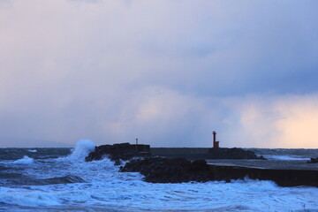 冬の日本海の荒波と小さな赤い灯台