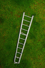 A silver ladder laid diagonally on a vibrant green grass field with some brown patches © Rifqi Muflih