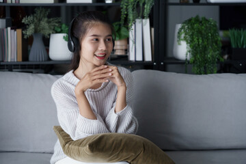 Fototapeta premium Asian woman sits on sofa listening to music in living room