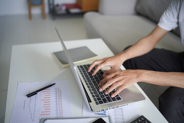 Man typing on laptop by two hands, He sitting on sofa in living room at home