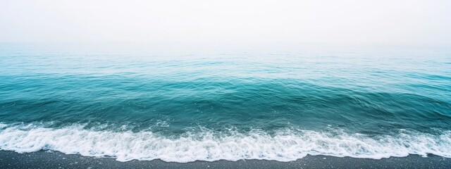 Obraz premium Tranquil coastal landscape capturing the serene beauty of calm ocean waves gently lapping against the shore under a hazy sky