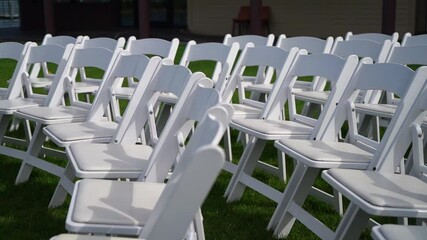 Rows of white folding chairs are arranged on a lush green grass lawn, perfect for an outdoor event such as a wedding or ceremony. The seating is prepared for guests to sit comfortably