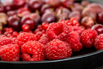 Tasty fresh ripe raspberry, red currant, gooseberry. Nutrients, Healthy berry texture on dark background. Red summer berries on black plate, food photography for food blog