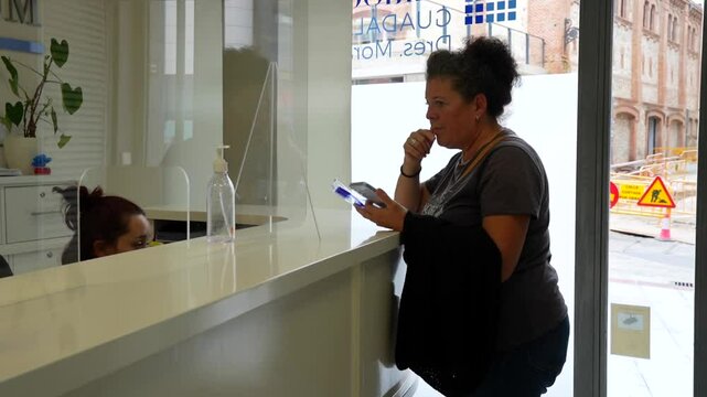 Woman waiting at dental clinic reception, using phone to check available dates for next visit