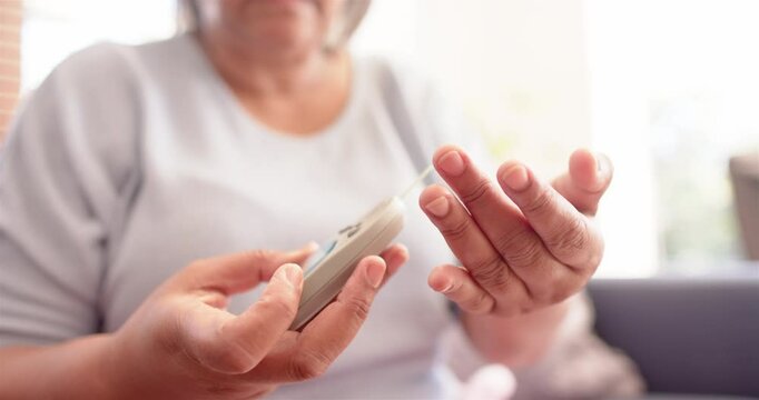 Senior woman checking blood sugar level using glucometer at home - Powered by Adobe