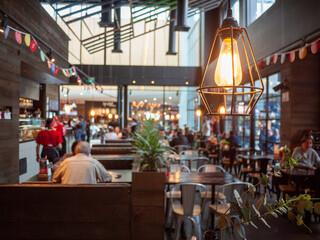 Close of an industrial-style pendant lighting bulb against a blurred view of a bustling casual...