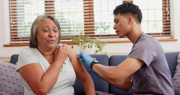 Administering vaccine, male nurse giving injection to senior woman at home