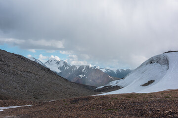 Beautiful glacier with view to big snow mountain range with sunlit pointy peak under clouds in blue...