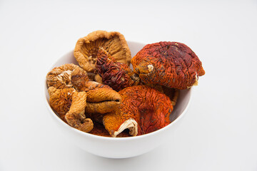 Dried red fly agaric mushrooms in a white bowl on a white background.