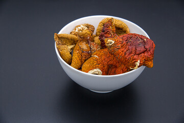 Dried red fly agaric mushrooms in a white bowl on a dark background.
