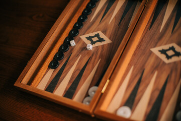 A close-up image of a backgammon board in use, featuring black and white game pieces and two dice on the wooden playing surface. The photo showcases the intricate design of the game board.