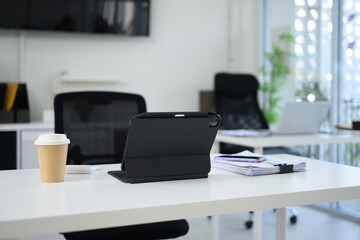 White office desk with digital tablet, a takeaway coffee cup, and stack of documents