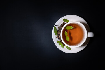 A cup of warm tea and tea leaves on a black background flatlay copyspace