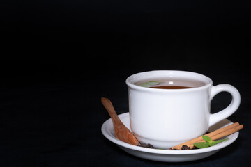 A cup of tea, a wooden spoon and tea leaves at black background