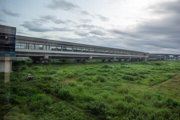 Airport train station spans above lush green fields under a cloudy sky. The infrastructure showcases contemporary design in transportation and urban planning amidst a natural setting.