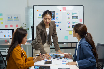Three asian businesswomen are analyzing financial charts and graphs, discussing company performance and planning strategies during a productive meeting in a modern office