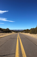 Naklejka premium A cinematic view of a long, desolate road stretching into the horizon on a clear day, under a vast blue sky. Captured with muted colors, a flat horizon line, for a dramatic view.