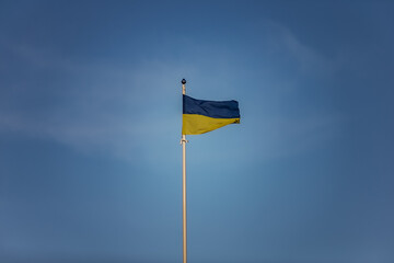 Dramatic colored Ukrainian flag high in flag post over dark and dramatic but blue skies. Flag as symbol for democracy and people willingness to fight