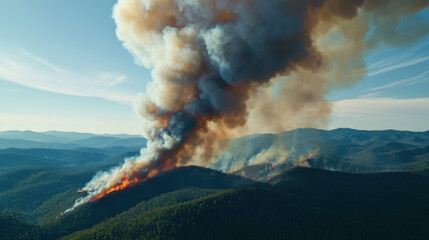 Fototapeta premium A vast landscape is engulfed in smoke from a forest fire, with flames visible on the hillside under a clear blue sky.