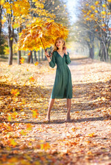 Beautiful slim girl with long red hair holds an umbrella made of maple yellow leaves and walks in the autumn park. Autumn season. Art portrait. Art photography.