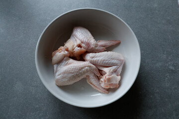 Raw chicken wings in a white bowl on the counter.