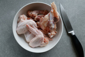 Raw chicken pieces in a white bowl on the counter, with a knife beside them.






