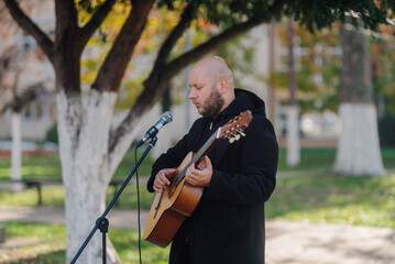 Street musician playing acoustic guitar and singing into microphone in park