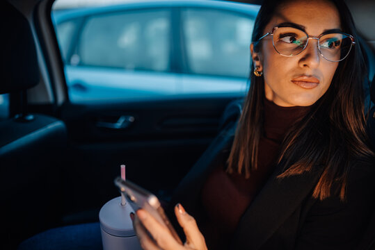 Businesswoman using smartphone and looking out window in car