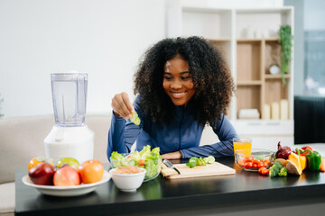 Smiling woman in a modern kitchen with fresh fruits, vegetables, blender, and orange juice,...