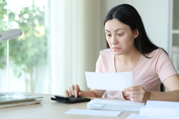 Perplexed asian woman checking receipt at home