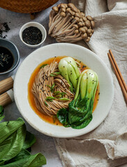 bowl of soba noodles in spicy broth with baby bok choy, surrounded by fresh mushrooms, ginger