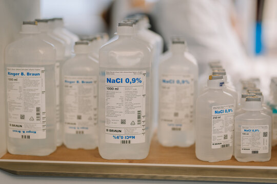Close-up of saline solution bottles labeled NaCl 0.9% and Ringer B. Braun, used for medical purposes, placed on a shelf in a hospital.