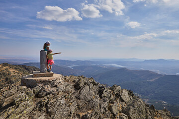Daughter and mother standing on top of a very high mountain on the plateau pointing fingers at the distant horizon, in Madrid, Spain
