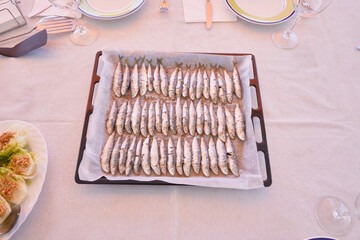 Baking tray full of small roasted sardines on a white tablecloth ready to serve and eat