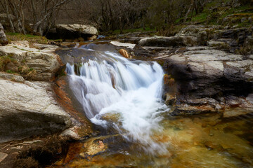Small river cascade with smooth effect due to long exposure between trees in autumn
