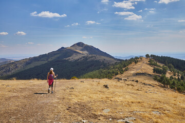 Woman from behind hiking along the mountain ridge towards a peak on the distant horizon, in Madrid, Spain
