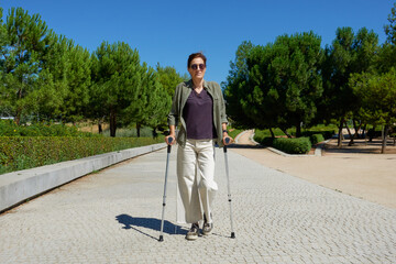 Woman walking with crutches on a cobblestone walk in an outdoor park in a city