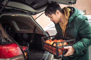 Man loading crate of oranges in car trunk at parking lot