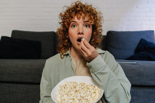 Surprised woman eating popcorn at home