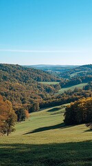 Obraz premium Scenic autumn valley landscape with rolling hills and colorful foliage under a clear blue sky.