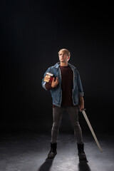 young student in a denim jacket and maroon sweater stands confidently in a studio, holding books...